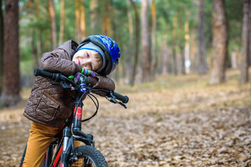 Fototapeta na wymiar Happy kid boy of 3 or 5 years having fun in autumn forest with a bicycle on beautiful fall day. Active child wearing bike helmet. Safety, sports, leisure with kids concept.