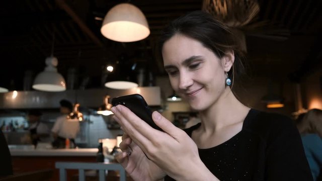 Young smiling woman sitting in cafe and using the smartphone. Attractive female chatting in social networks with friends