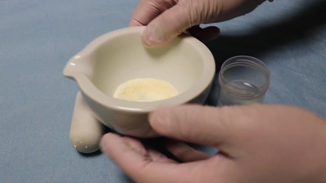  The hands  wearing rubber gloves poures  medicines into the flask with water.