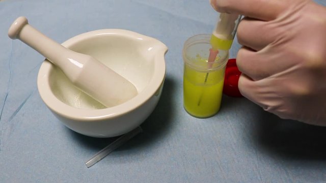 The hands  wearing rubber gloves   fills the syringe and  and covers the needle.