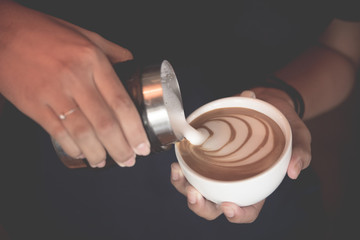 Hand of barista pouring cream to coffee for making latte art