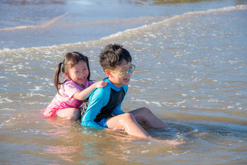 Young Asian siblings laughing happily after being hit by the sea waves while sitting by the beach
