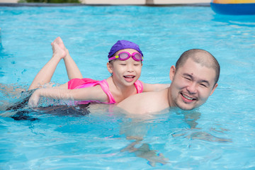 Little asian girl smiling happily on her father back in swimming pool