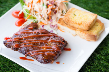 Close up view of pork barbecue ribs with barbecue sauce that served with garlic bread and vegetable salad.
