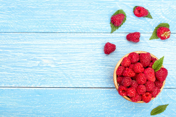 Raspberries in a bowl on the blue wooden background with copy space for your text. Top view