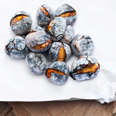 Roasted chestnuts served on white and brown craft paper with copy space. Delicious grilled  chestnuts on old wooden table close up.