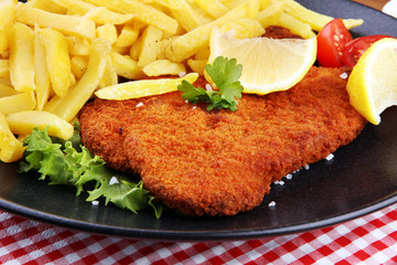 Dish of Wiener schnitzel and French fries served with sauces and salad on rustic wooden table