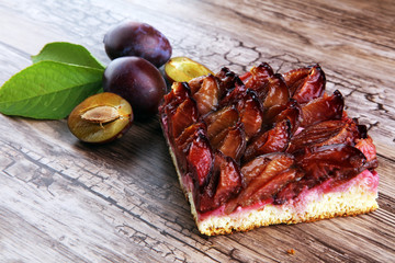 rustic plum cake on wooden background with plums around