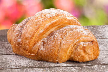 croissant sprinkled with powdered sugar on a wooden board with a blurry garden background