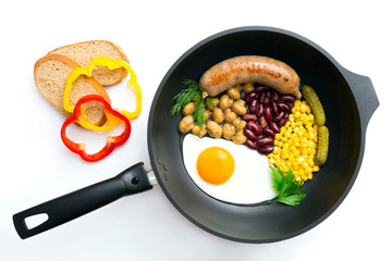 Breakfast in a frying pan.
Top view of a black frying pan with egg, mushrooms, beans, corn and cucumbers on white background. Sliced bread and capsicums are on the white surface.