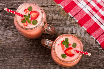 Glass of strawberry yogurt or smoothie with mint leaves on old wooden background. Top view