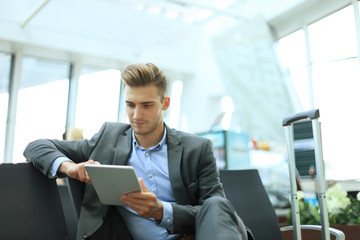 Businessman using digital tablet in airport departure lounge.