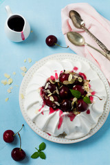 Homemade meringue cake Pavlova with whipped cream, fresh cherry and  sauce  on light concrete texture background.Selective focus. Top view, space