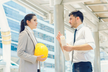 Obraz premium Engineer holding safety helmet and holding drawing discuss in building project planning, working together, concept of business negotiation and deal benefit.