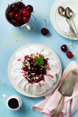 Homemade meringue cake Pavlova with whipped cream, fresh cherry and  sauce  on light concrete texture background.Selective focus. Top view, space