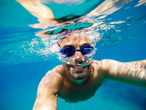 Charming young man is taking a selfie and smile underwater.