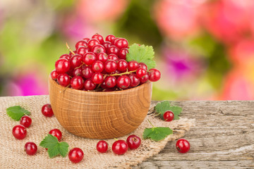 Red currant berries in wooden bowl on wooden table with blurry garden background