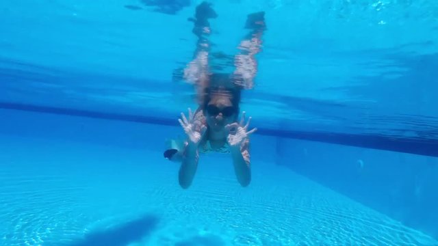 Teen girl swims under water and shows gesture that everything is fine