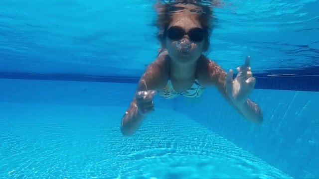 Teen girl swims under water and shows gesture symbol of heart