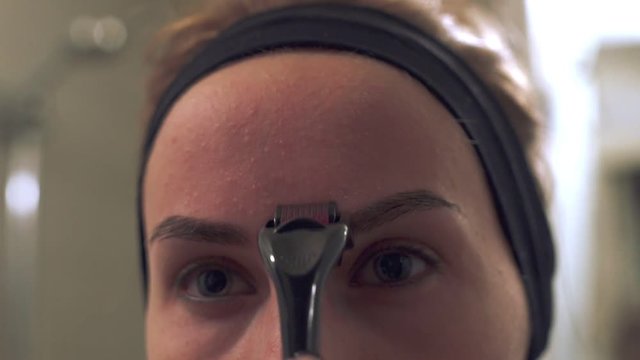 Close up young woman using a derma roller for micro needling therapy face.