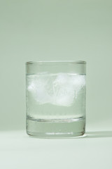 Ice drinking water glass on table over green.