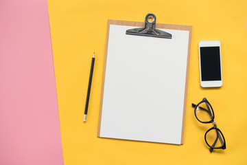 Flat lay design of Blank clipboard, smartphone,pencil and glasses on pink and yellow background...