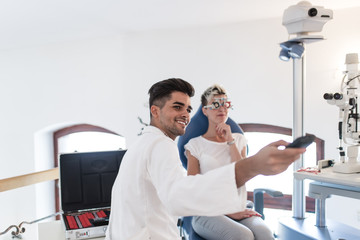 Fototapeta premium Male optometrist with trial frame checking patient's vision at eye clinic.