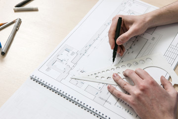 Architecture scheme with unrecognizable hands drawing on desktop of designer workplace
