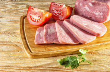 Ham and tomatoes lying on wooden background