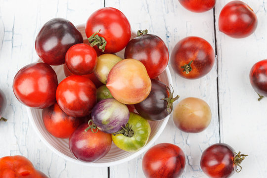 Different tomatoes in the bowl on the white wooden background