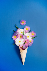 Waffle cone with chamomile flower bouquet on blue background. Flat lay, top view floral background.