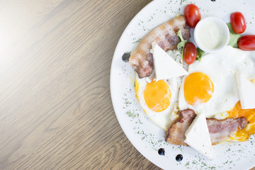 Fried eggs with bacon on the wooden table. Tomato and cheese on the side.