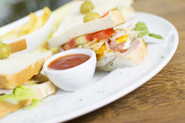 Club sandwich with chicken breast, bacon, tomato, cucumber, and herbs. French fries on the side.