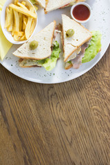Club sandwich with chicken breast, bacon, tomato, cucumber, and herbs. French fries on the side.