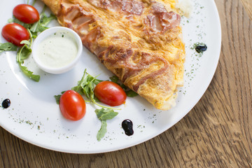 Scrambled eggs with ham on a plate on the wooden table. Tomato and sour cream on the side.