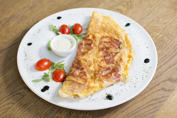 Scrambled eggs with ham on a plate on the wooden table. Tomato and sour cream on the side.