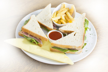 Club sandwich with chicken breast, bacon, tomato, cucumber, and herbs. French fries on the side.