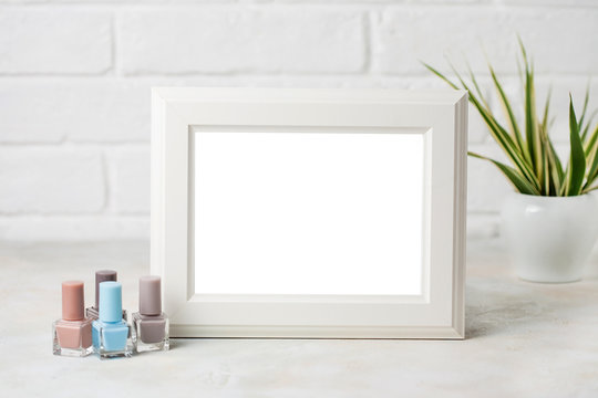White wooden frame with copyspace and cosmetic brushesh and nail polish. Fahion beauty mockup concept on white Brick wall background.