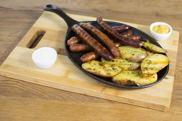 Grilled sausages and potatoes on wooden cutting board. Mustard on the side.