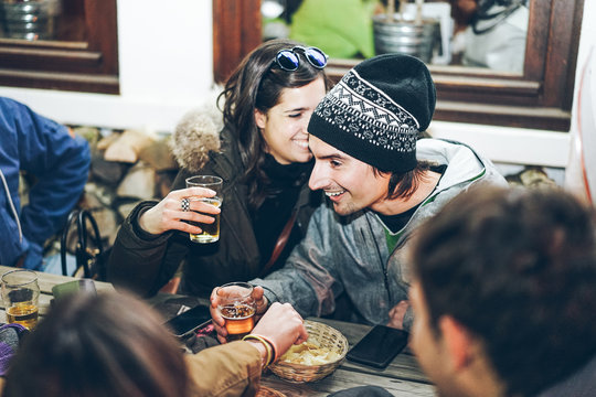 Happy rich friends toasting beers at chalet pub restaurant in mountains on evening time - Young people having fun in winter vacation - Friendship concept - Soft focus on woman face - Warm filter