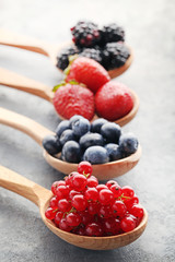 Ripe and sweet berries in spoons on grey wooden table