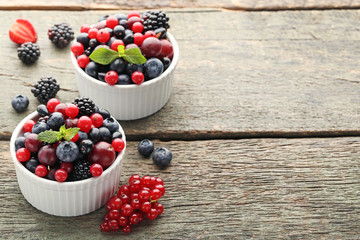 Ripe and sweet berries in bowls on wooden table