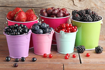 Ripe and sweet berries in buckets on wooden table