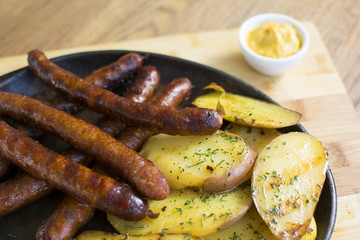 Grilled sausages and potatoes on wooden cutting board. Mustard on the side.