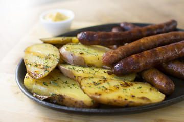 Grilled sausages and potatoes on wooden cutting board. Mustard on the side.