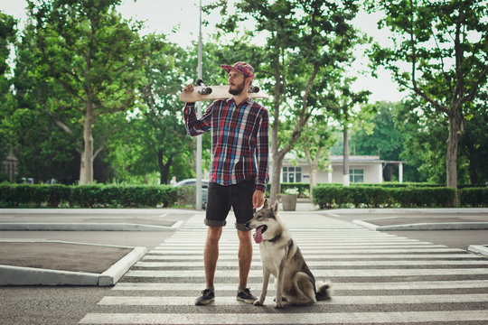 Young hipster man with skateboard and siberian husky dog standing on street road