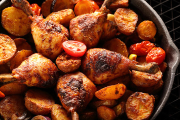 Roasted chicken legs with baked potato on frying pan