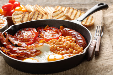 English Breakfast with sausages, grilled tomatoes, egg, bacon, beans and bread on frying pan.