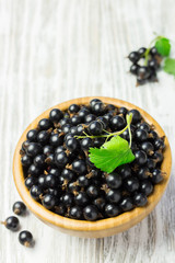 Black currant in a wooden bowl on white shabby wooden background. Selective focus, space for text.