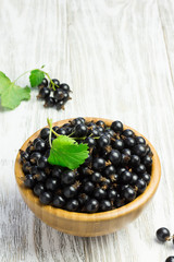 Ripe black currant in a wooden bowl on white shabby wooden table. Selective focus, space for text.